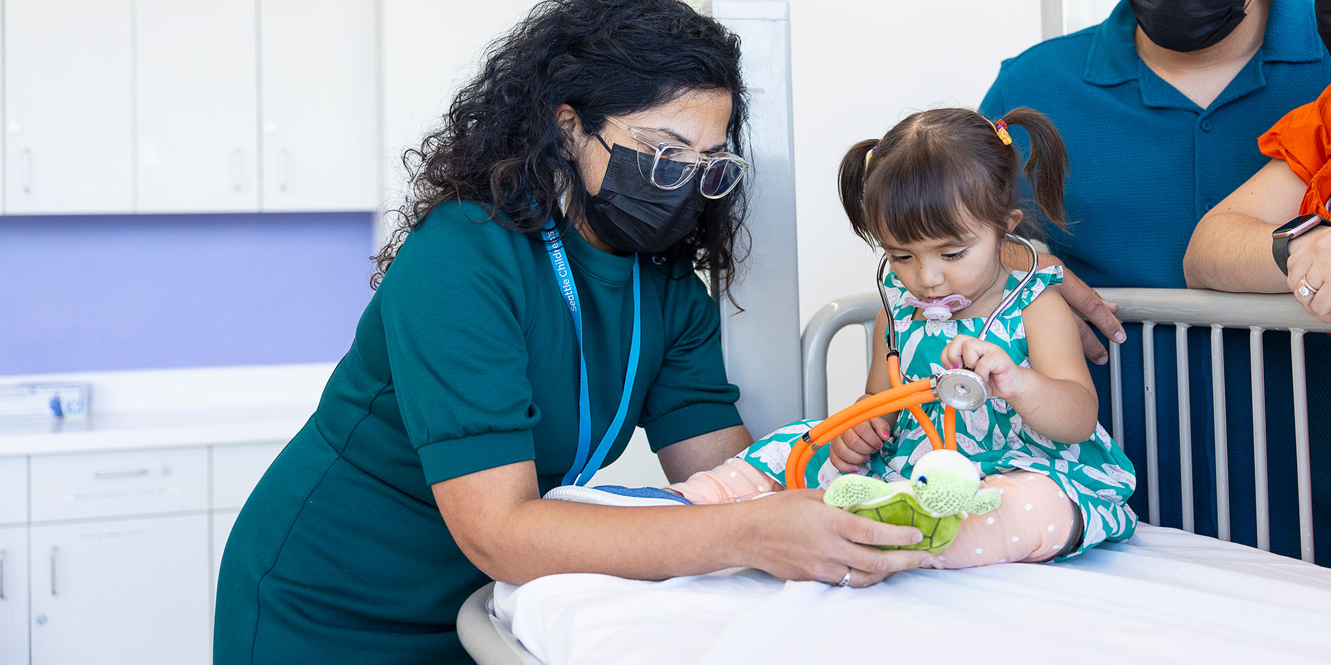 A doctor holds a stuffed toy turtle for a young girl holding a stethoscope