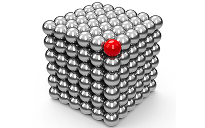 A cube formed by small silver metallic spherical magnets, with a single red magnet on top.